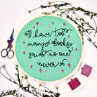 Embroidery hoop with text 'I have too many books, said no one ever.' surrounded by flowers and sewing supplies.